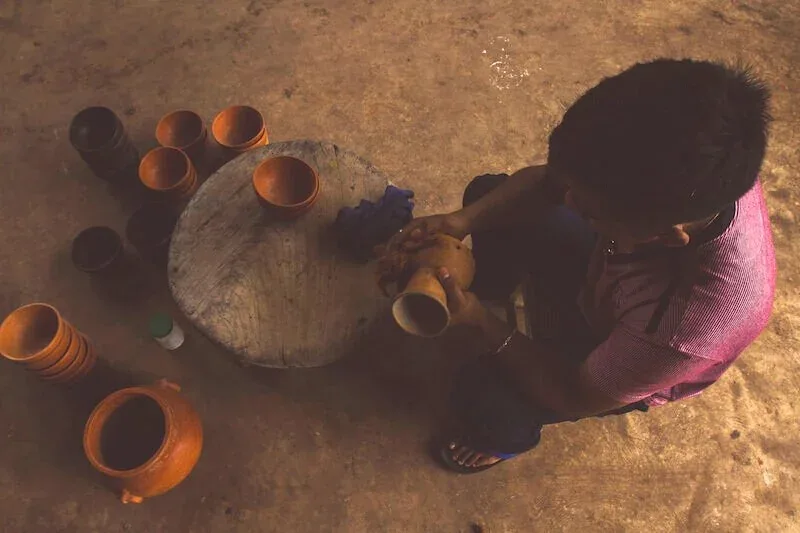A boy filling clay pots on the ground at the workshop