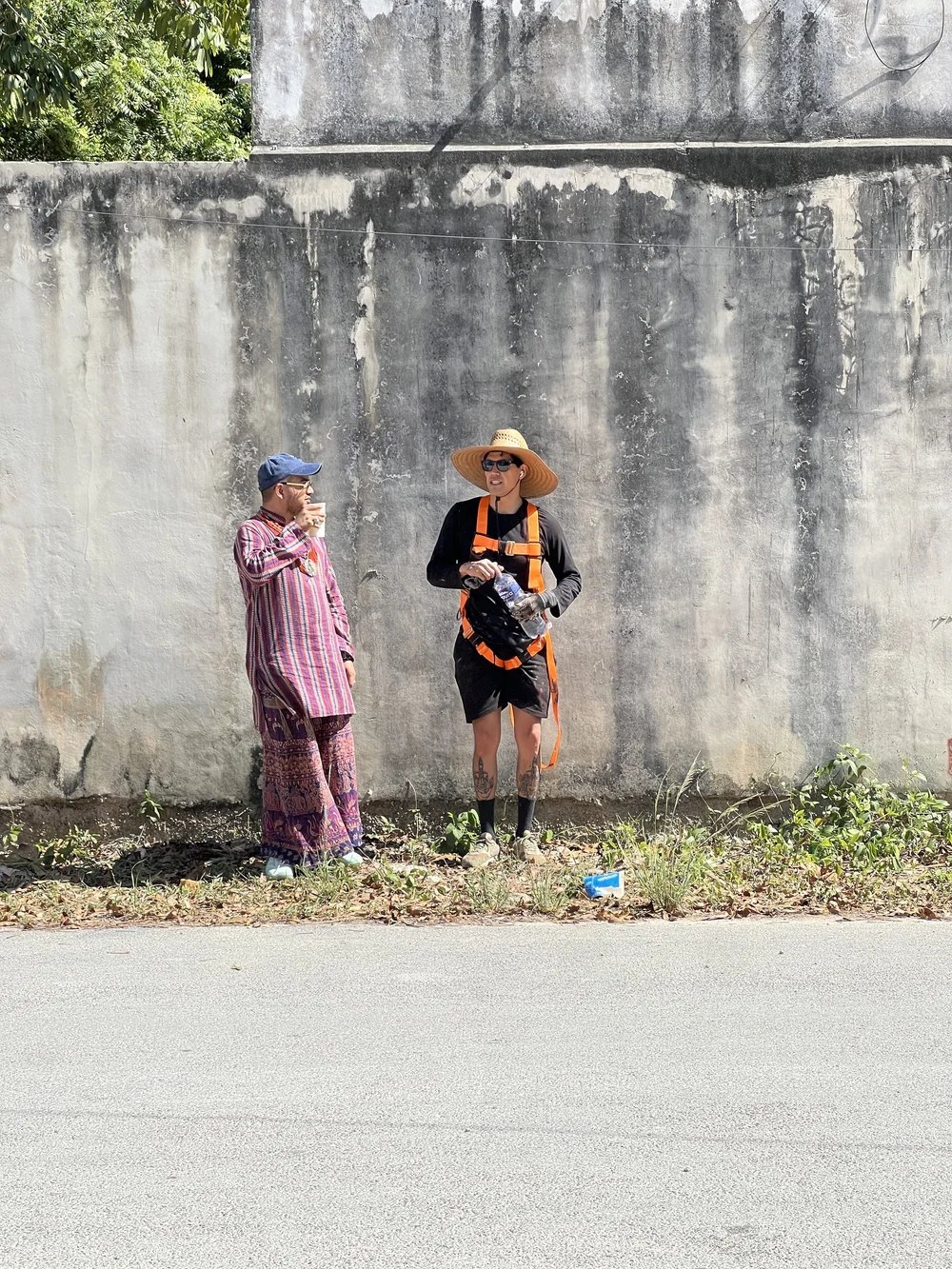 Two members of the Horizontes Mexicanos team pause beside a weathered concrete wall in Tulum during a mural production day.
